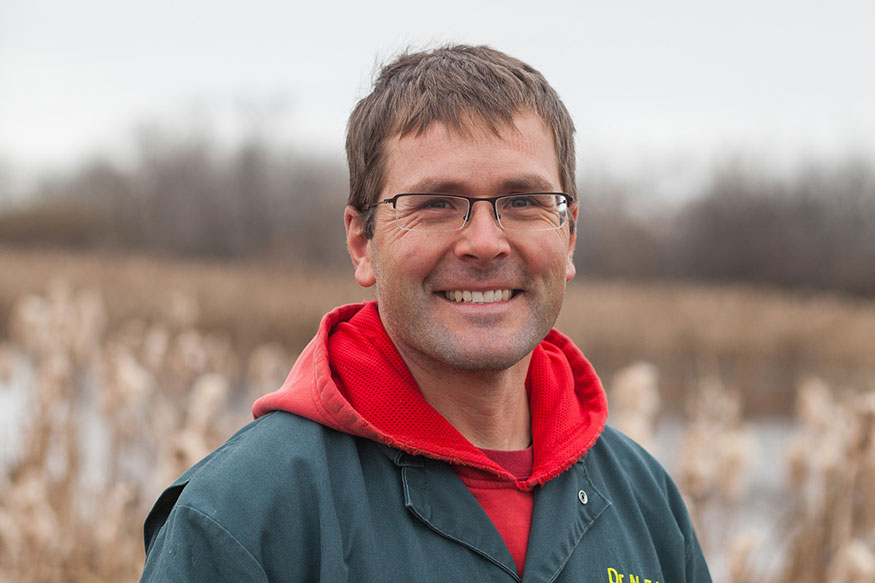 Dr. Nathan Erikson is standing outside in a field in coveralls and a red hoodie