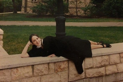 Laying on a stone wall on USask campus in convocation gown